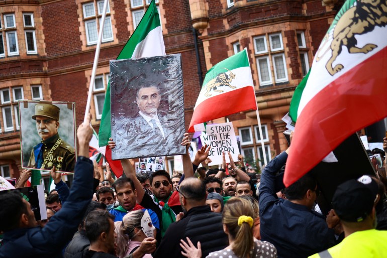 A man holds a portrait of Reza Pahlavi as others wave Iran flags at a crowded protest