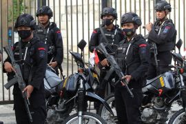 Indonesian police from the mobile brigade known as Brimob outside the court for the trial of three officers over their role in the stampede at a Malang football stadium that left 135 people dead. Thy are wearing black uniforms and helmets and have weapons.