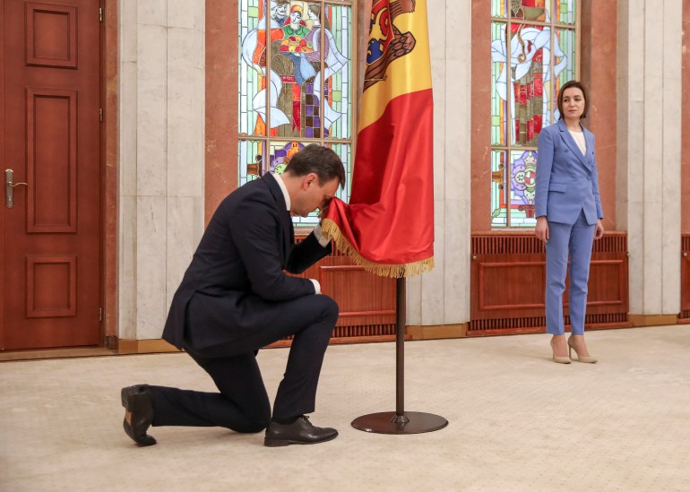 New Moldovan Prime Minister Dorin Recean kneels down in front of a state flag as President Maia Sandu stands nearby during an inauguration ceremony in Chisinau, Moldova, February 16, 2023. REUTERS/Vladislav Culiomza