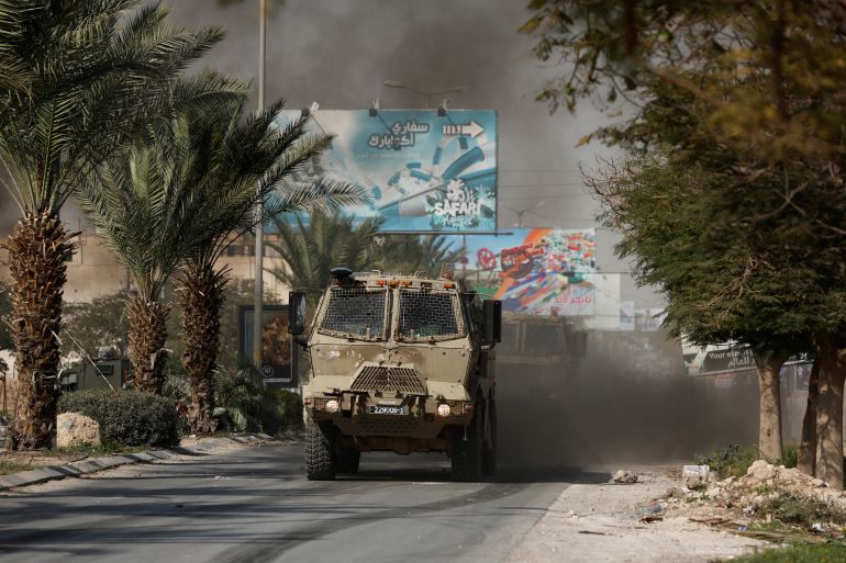 Israeli armoured vehicle drives through a street lined with palm trees