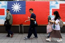 People in Taipei walk past a hoarding of a large Taiwan flag.