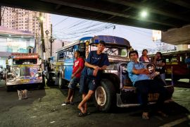 Three jeepney drivers leaning against the bonnet of one of a parked jeepney. It's parked
