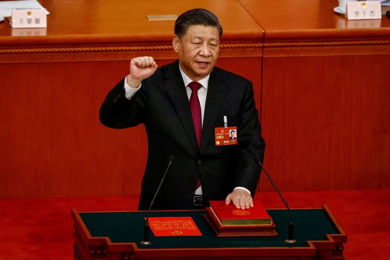 Chinese President Xi Jinping takes his oath of office. He has his left hand on the Chinese constitution and his right hand in a fist.He is in the Great Hall of the People.