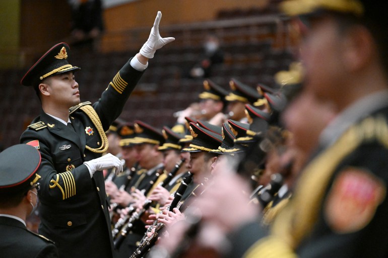 The PLA band in full regalia practises for the NPC closing session. The conductor has his left arm raised. He's wearing white gloves.