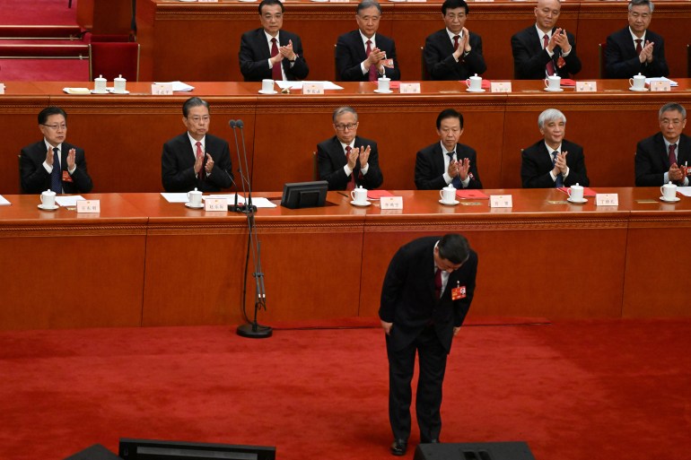Xi Jinping bows before he begins his closing speech. Delegates seated behind him applaud. 