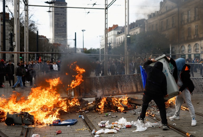 People carry an object next to a fire during clashes at a demonstration to protest the use by French government of the article 49.3, a special clause in the French Constitution, to push the pensions reform bill through the National Assembly without a vote by lawmakers, in Nantes, France, March 18, 2023. 