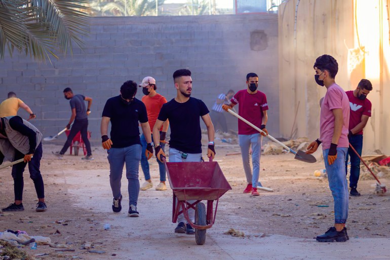 A photo of Laith pushing a wheelbarrow with people using shovels and digging all around him.