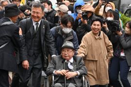 Iwao Hakamada attends court in Tokyo with his family and supporters. He is a wheelchair. and wearing glasses His sister is next to him and smiling as she walks.