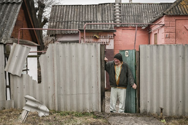 An elderly man stands at the entrance of his house