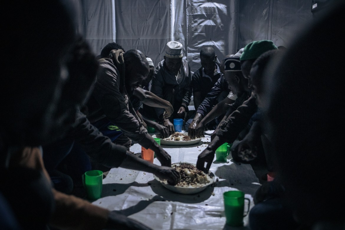 Muslims break the Ramadan fast by digging in to platters of rice and beans. A dim overhead light provides just enough illumination in the makeshift structure.