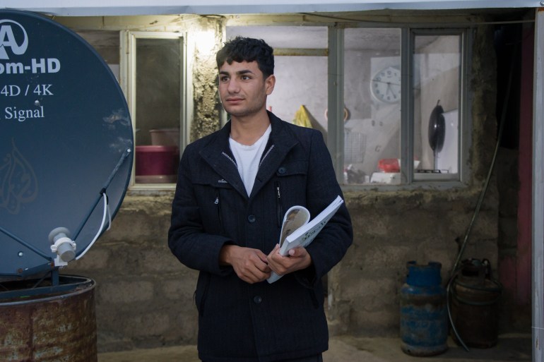 A photo of Nazar standing in the camp holding his high school book.