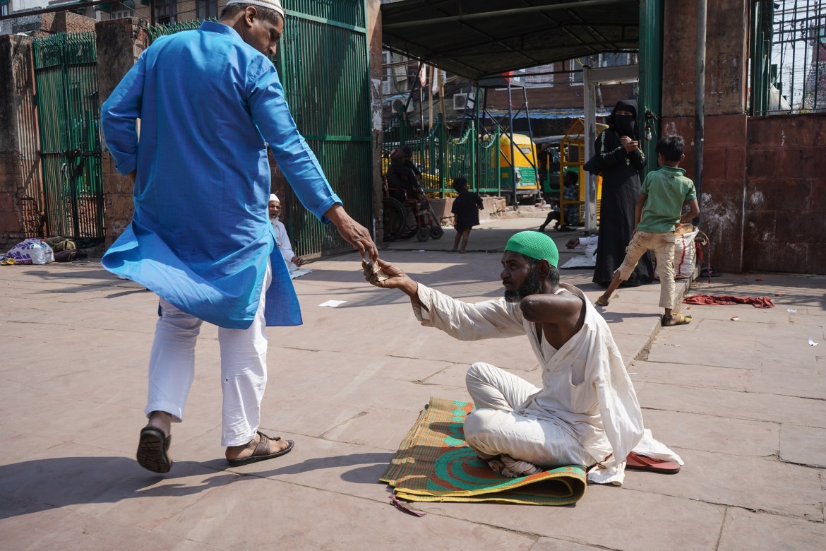 A Muslim man gives alms to a beggar at Jama Masjid's gate. During this month, Muslims consider it more rewarding to help the poor and destitute.