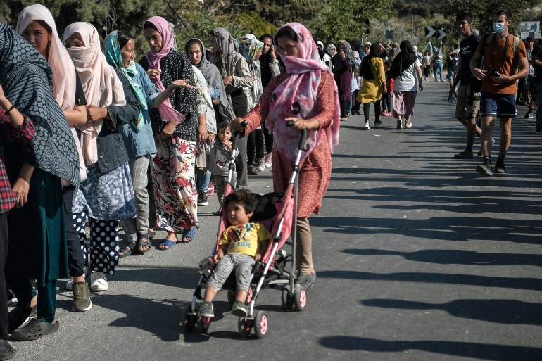 Asylum seekers queue for food distribution along the roadside where thousands are living without shelter and exposed to the elements following the burning down of their camp, near the Kara Tepe camp on the island of Lesbos on September 13, 2020. A woman pushing a stroller with a small child in it is in the centre of the image.