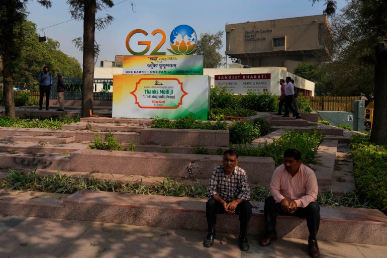 People sit around a G20 logo at a crossing in New Delhi