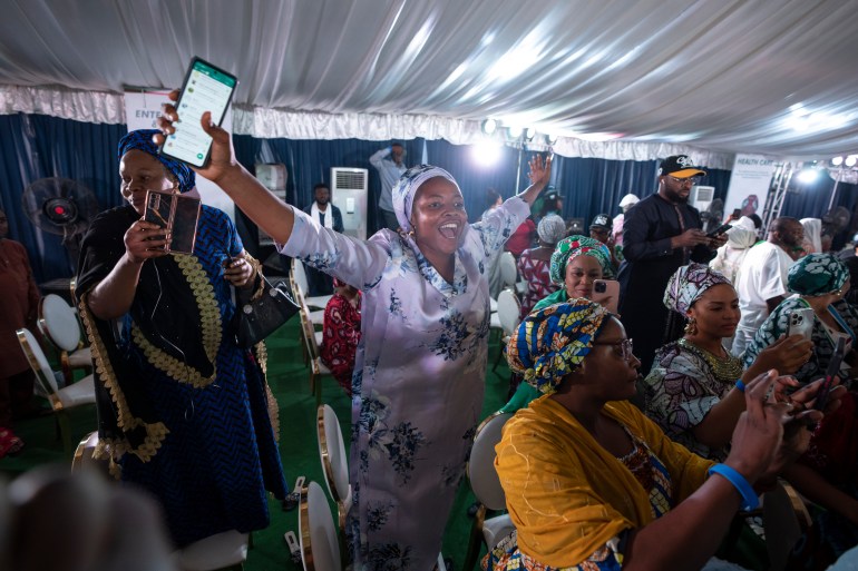 Bola Tinubu's supporters celebrate his victory. A woman has her arms outstretched with a phone in one hand and is laughing and smiling. She is surrounded by other supporters who are celebrating 