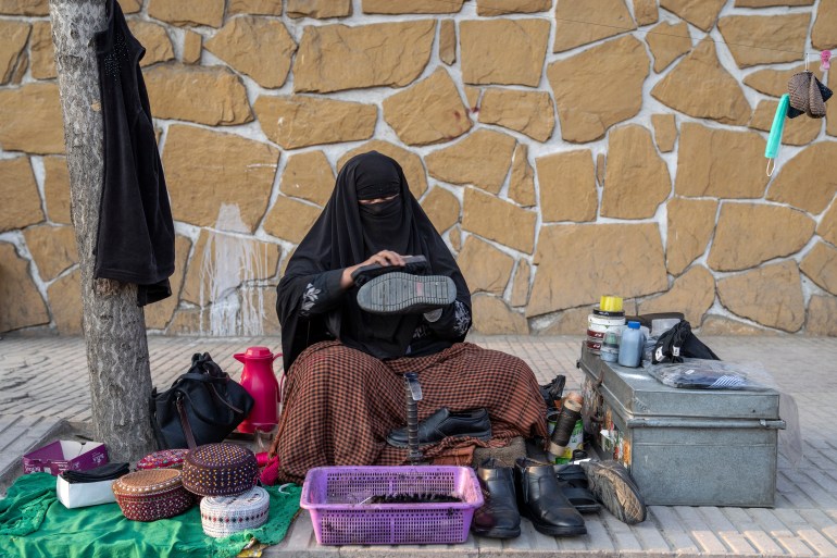 An Afghan woman cleans a customer's shoes in the street in Kabul, Afghanistan, March 5, 2023 [Ebrahim Noroozi/AP Photo]
