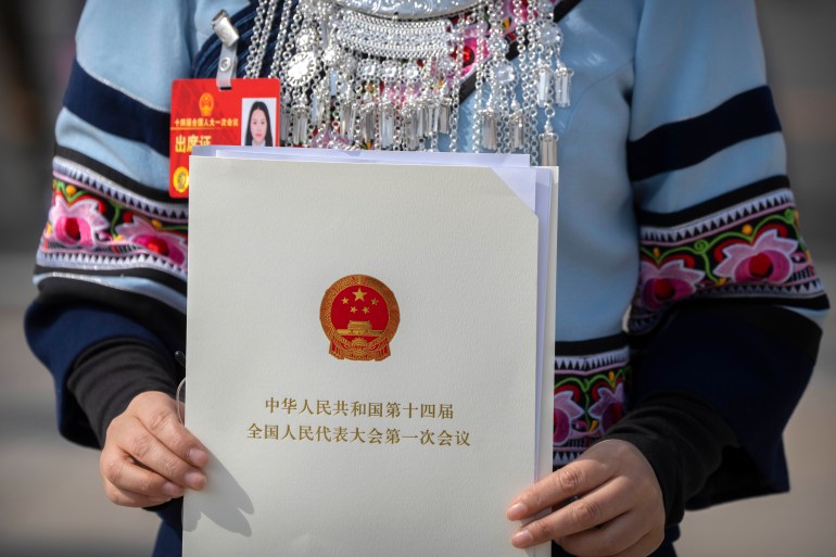 A female delegate in the traditional outfit of an ethnic minority group holds up a ballot paper at the NPC