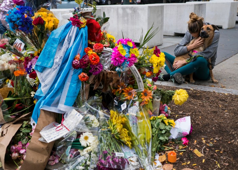 A makeshift tribute of flowers honours the dead in a 2017 attack. A woman is sitting close to the site, hugging her dog in her lap and burying her face in its fur.