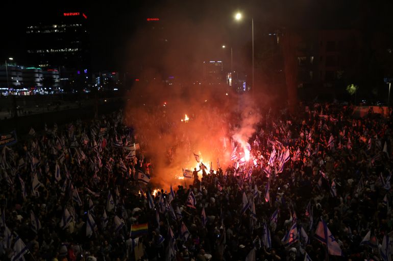 Israeli protesters light a bonfire on a Tel Aviv highway. Hundreds of protesters can be seen silhouetted as they surround the bonfire.