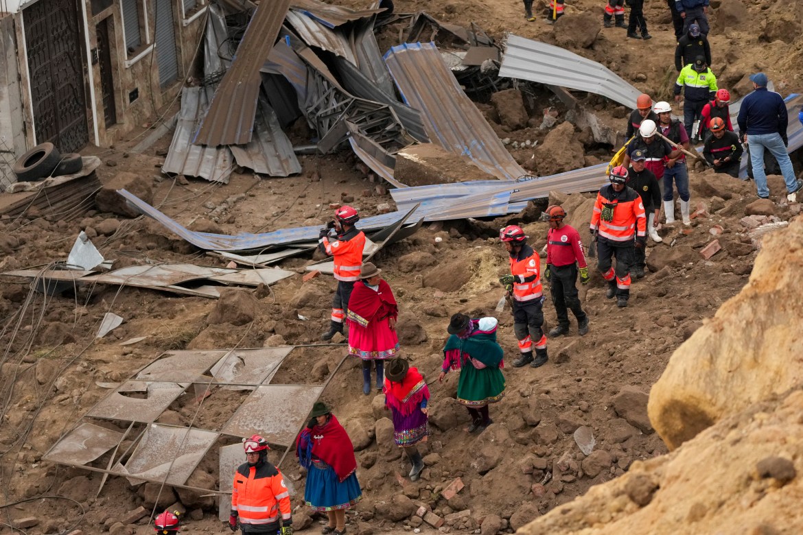Rescue workers and residents walk amid the debris after a deadly landslide that buried dozens of homes in Alausi, Ecuador