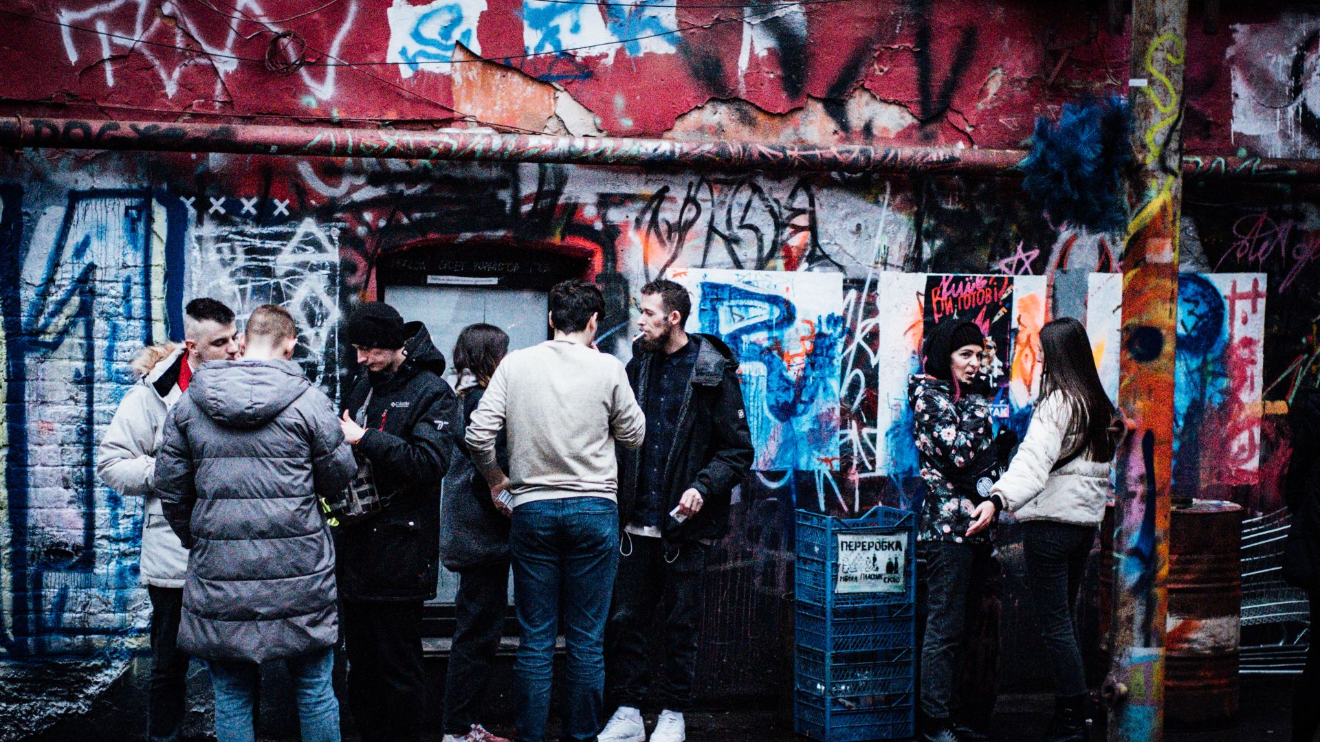 A photo of people standing outside, in front of a wall filled with graffiti.