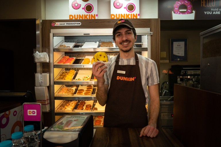 Man wearing a dunkin donuts apron holds up a donut 