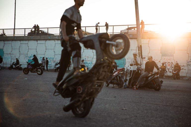 Youngsters do tricks on their motorbikes against a setting sun
