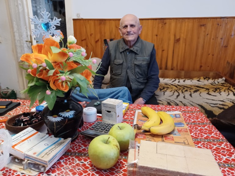 A photo of Ivan Capan sitting st a table with two bananas, pears and pills on the table in front of him.