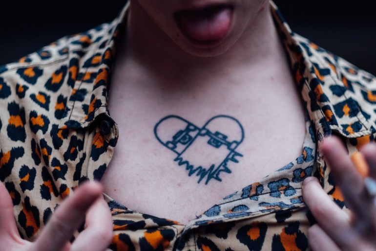 A photo of someone showing the tattoo below their neck of a heart with jagged edges at the bottom and locks at the top.