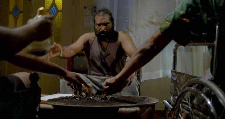 A scene from the Tamil language film Poochandi. It shows a bare-chested man through two outstretched hands
