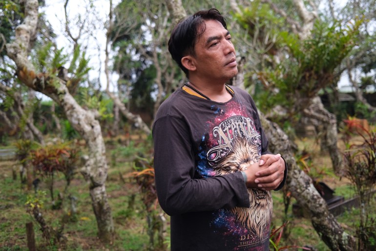 Wiyanto standing in the cemetery where his son is buried. He's wearing a black, long-sleeved t-shirt.