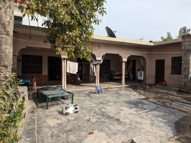 A photo of the outside of Zubeidas home with clothes hanging, a table and a child walking behind the table.