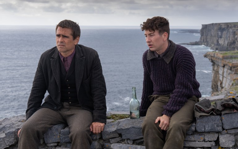 Colin Farrell and Barry Keoghan sit on a stone fence overlooking the sea