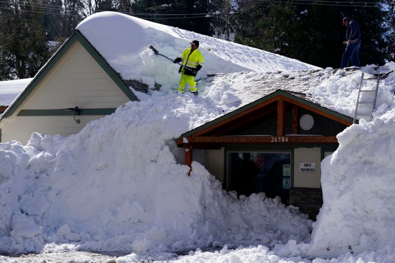 A worker shovels snow off of the roof of a building covered in snow