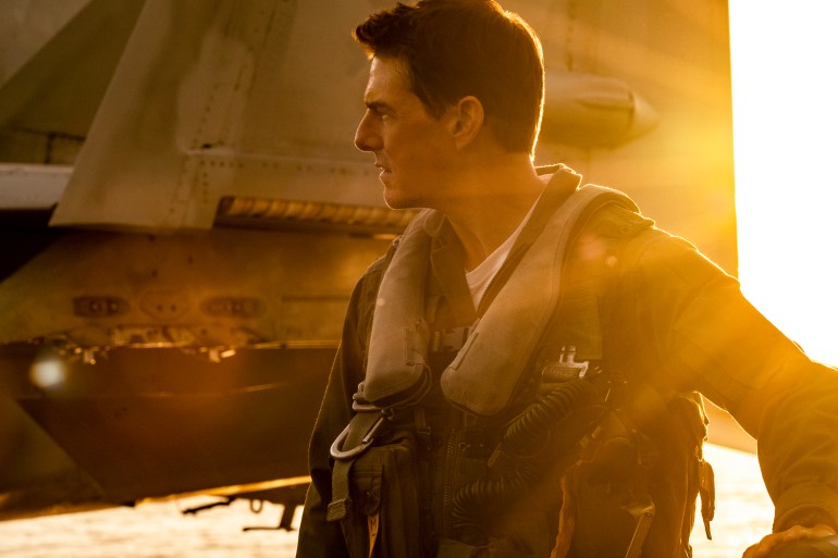Tom Cruise stands adjacent to a military jet, as the setting sun pours over his shoulder in this shot from the film Top Gun: Maverick.