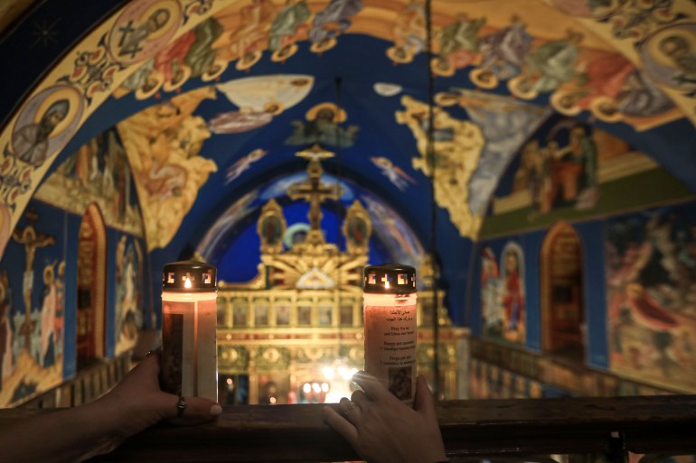A view of two hands holding blessing candles against the richly painted ceiling of the church