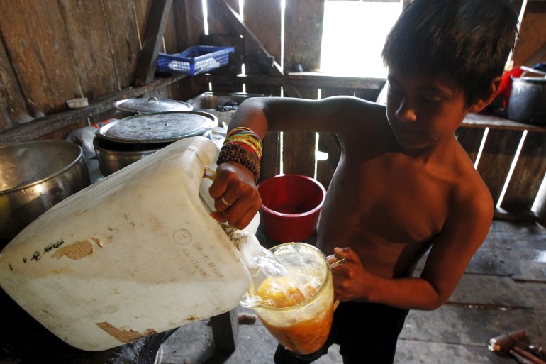 A Cofán boy pours water into a container filled with an orange substance in his home in Dureno