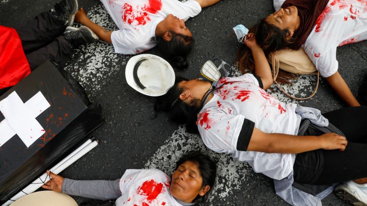 Protesters pretend to be dead on the concrete, wearing red-splattered white shirts. A fake coffin — black with a white cross — sits next to them.