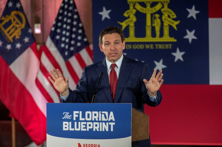 Ron DeSantis raises both hands at a podium labeled "the Florida blueprint"
