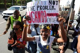 Women walk on a street in Cape Town to oppose Uganda's anti-LGBTQ law. One is carrying a placard above her head reading 'We are not the problem'