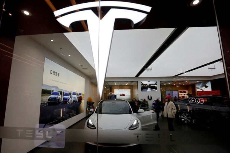 A Tesla logo on a window, with an electric vehicle behind it in a showroom