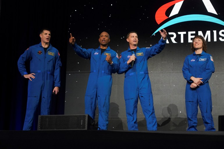 Four astronauts wave on stage at an event