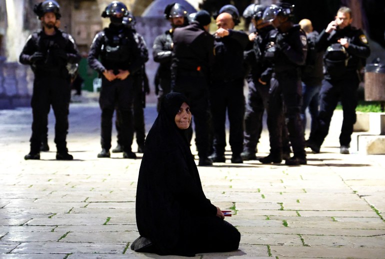 A Palestinian woman sits near Israeli border policemen in the Al-Aqsa compound,