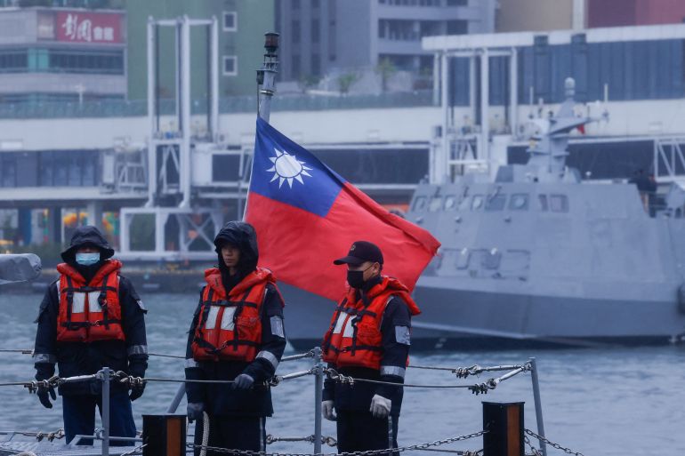 Two Taiwanese sailors at port. There is a Taiwan flag and a military ship behind them.