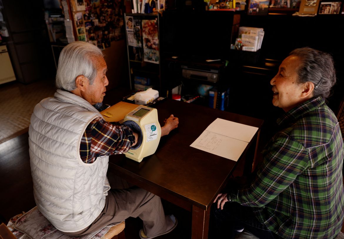 Mutsuhiko Nomura (left), 83, checks his blood pressure while his wife Junko Nomura, 80, writes down the reading on a notebook to keep record, at their home in Tokyo