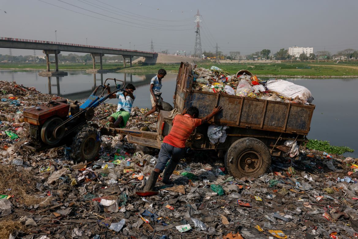 Workers dump waste into a landfill located just beside Dhaleshwari river, water from which flows into the Buriganga river