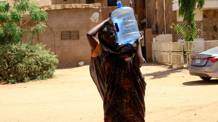 A woman carries a gallon of water in Sudan during fighting