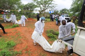 Kenyan forensic experts and homicide detectives, dressed in white personal protective equipment, carry the bodies of suspected members of a Christian cult to waiting vehicles as part of an investigation.