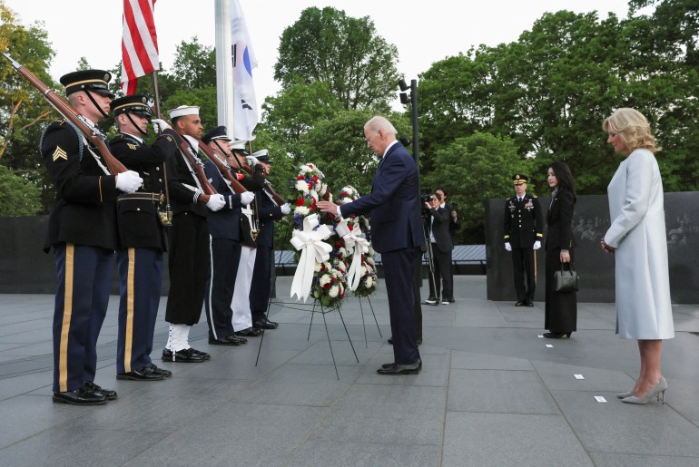 Joe Biden arranges a wreath with flowers, before a line of soldiers