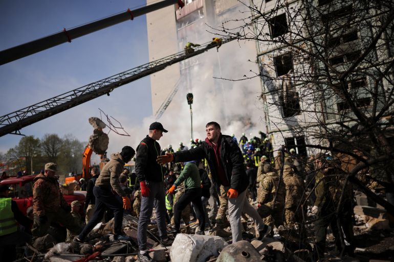 Local residents and rescuers work amidst the rubble at the site of a heavily damaged residential building hit by a Russian missile